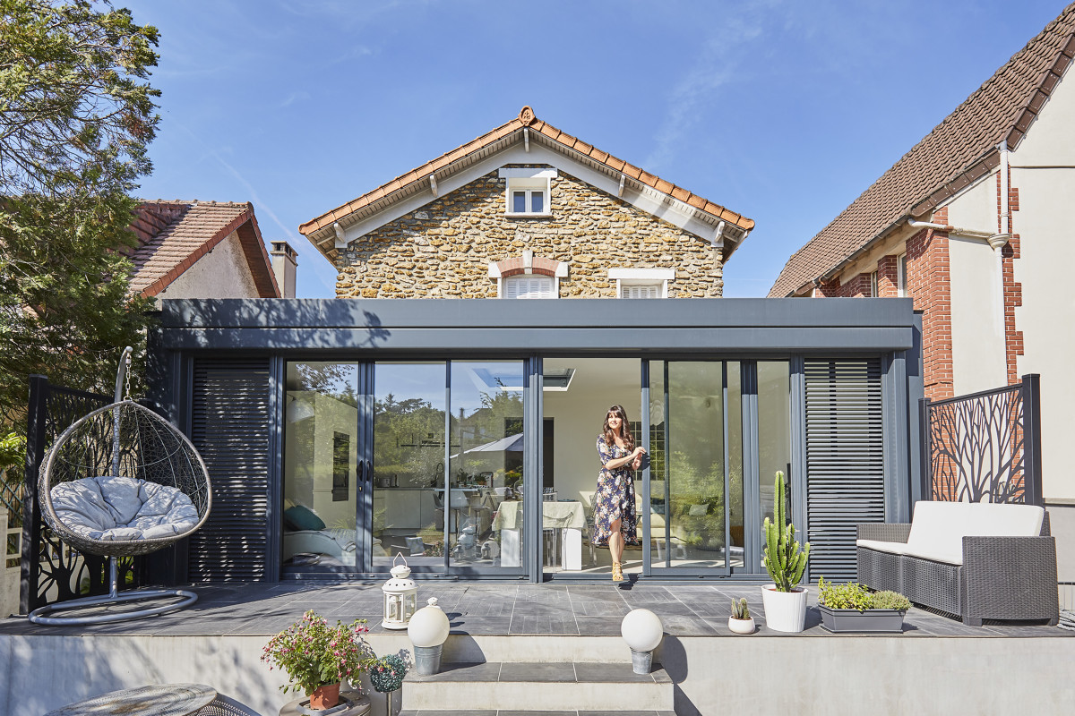 véranda moderne à toit plat devant vieille maison en pierre